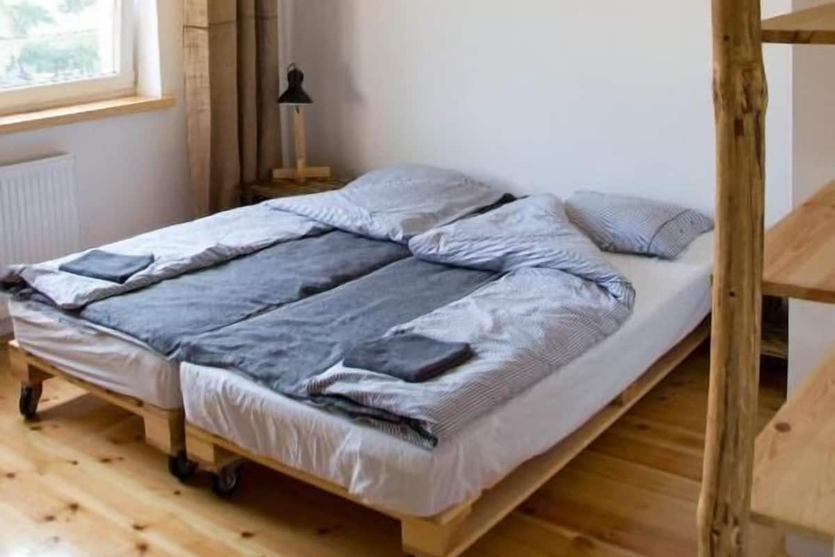 A single bed with a headboard, a window with curtains, a radiator, and a lamp on a wooden floor.