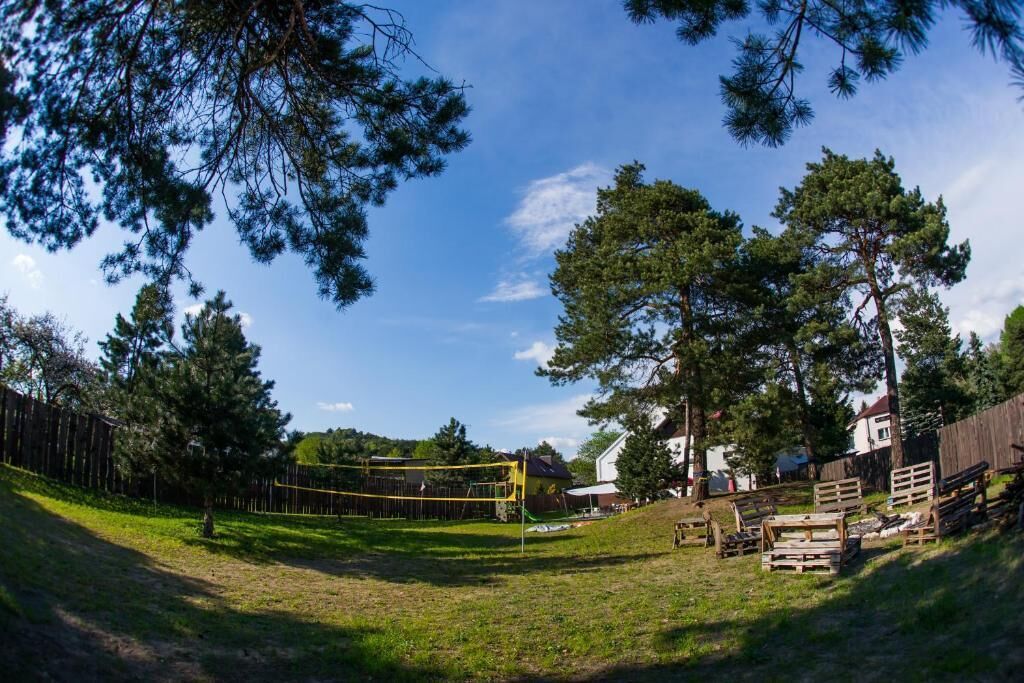 Un espace extérieur clôturé comprenant un filet de volley-ball, des bancs en bois et des arbres.