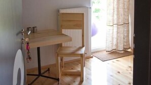 A room with a wooden desk, chair, radiator, and a window with curtains.