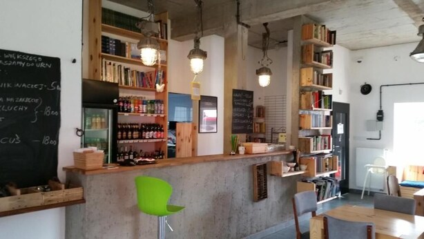 A bar area with shelves of bottles, a chalkboard menu, and a seating area with chairs.