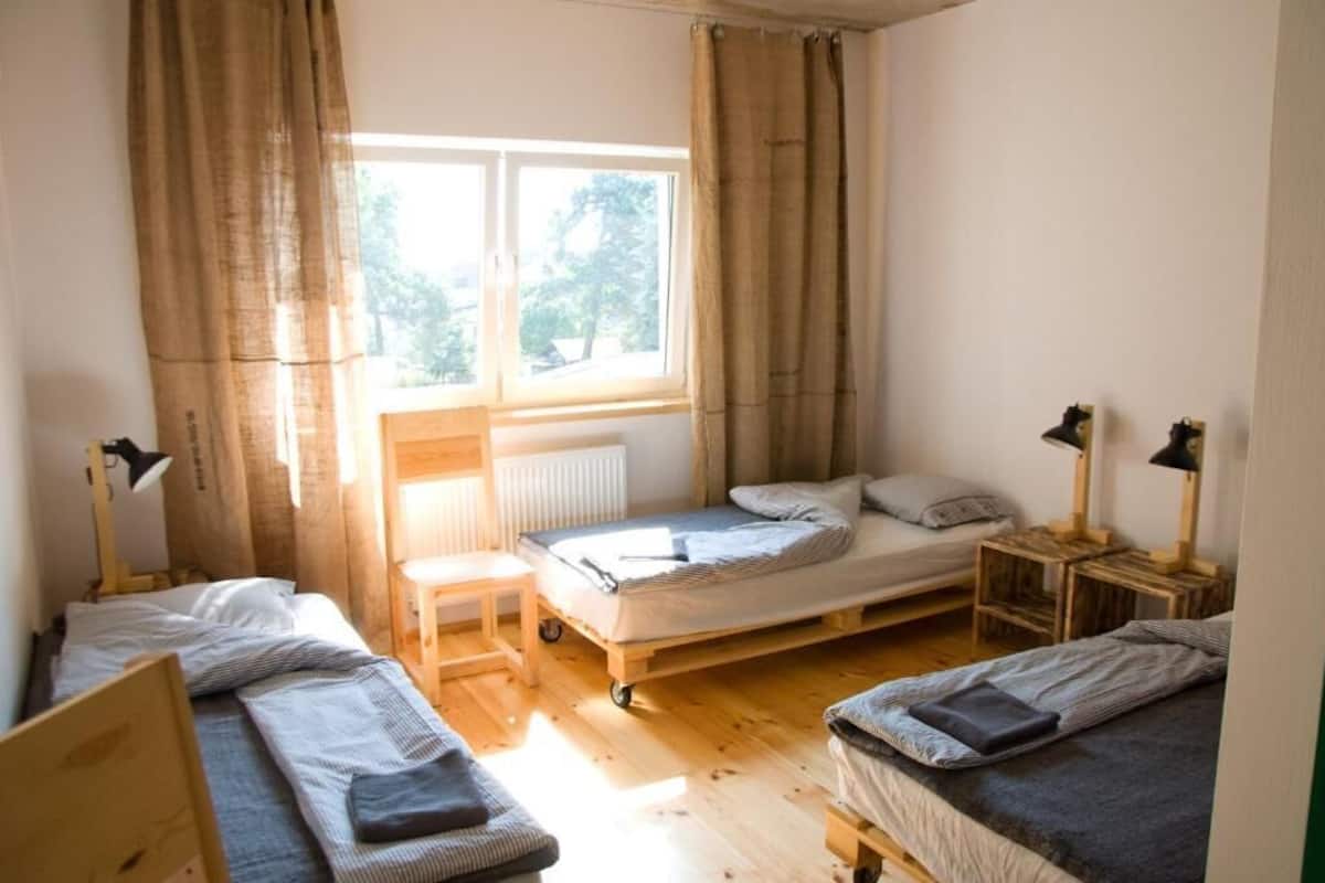 A room with a bed, two smaller beds, a window, and a radiator.