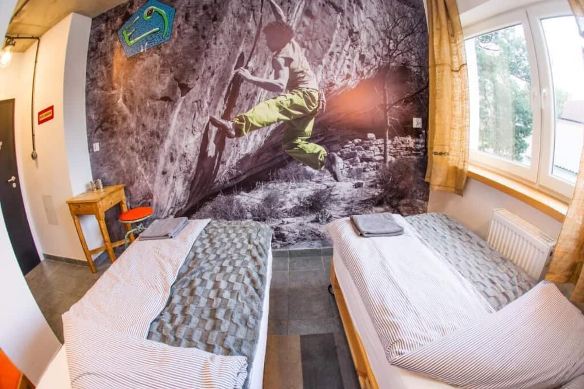 A room with two beds, a climbing wall mural, a small table, and a window with curtains.