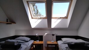 A room with two beds, skylights, a radiator, and a small table with a lamp.