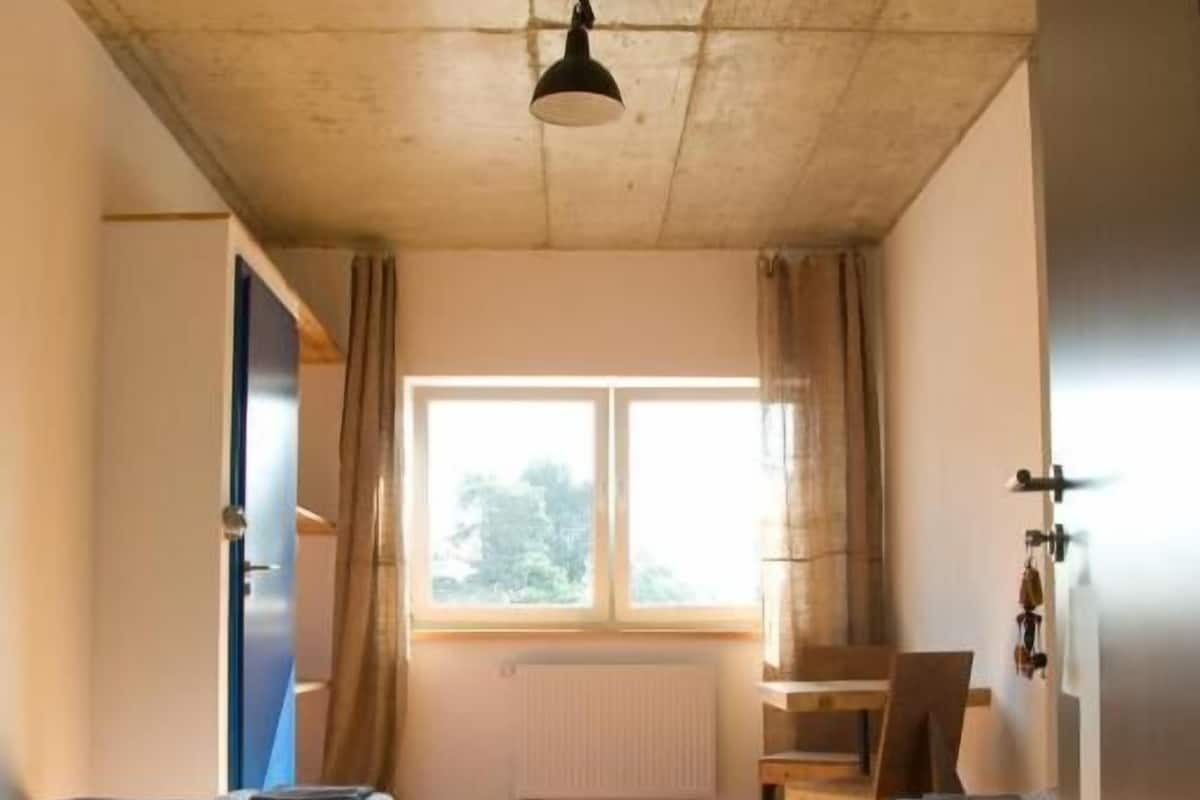A room with a wooden floor, a window with curtains, a desk, and two beds.