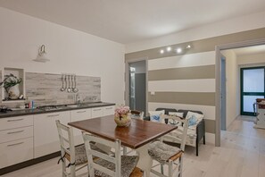 A modern kitchen with a dining area, featuring a wooden table, white chairs, and a vase with flowers. - GuestHost - Casa De Battè Apartment (Riomaggiore)