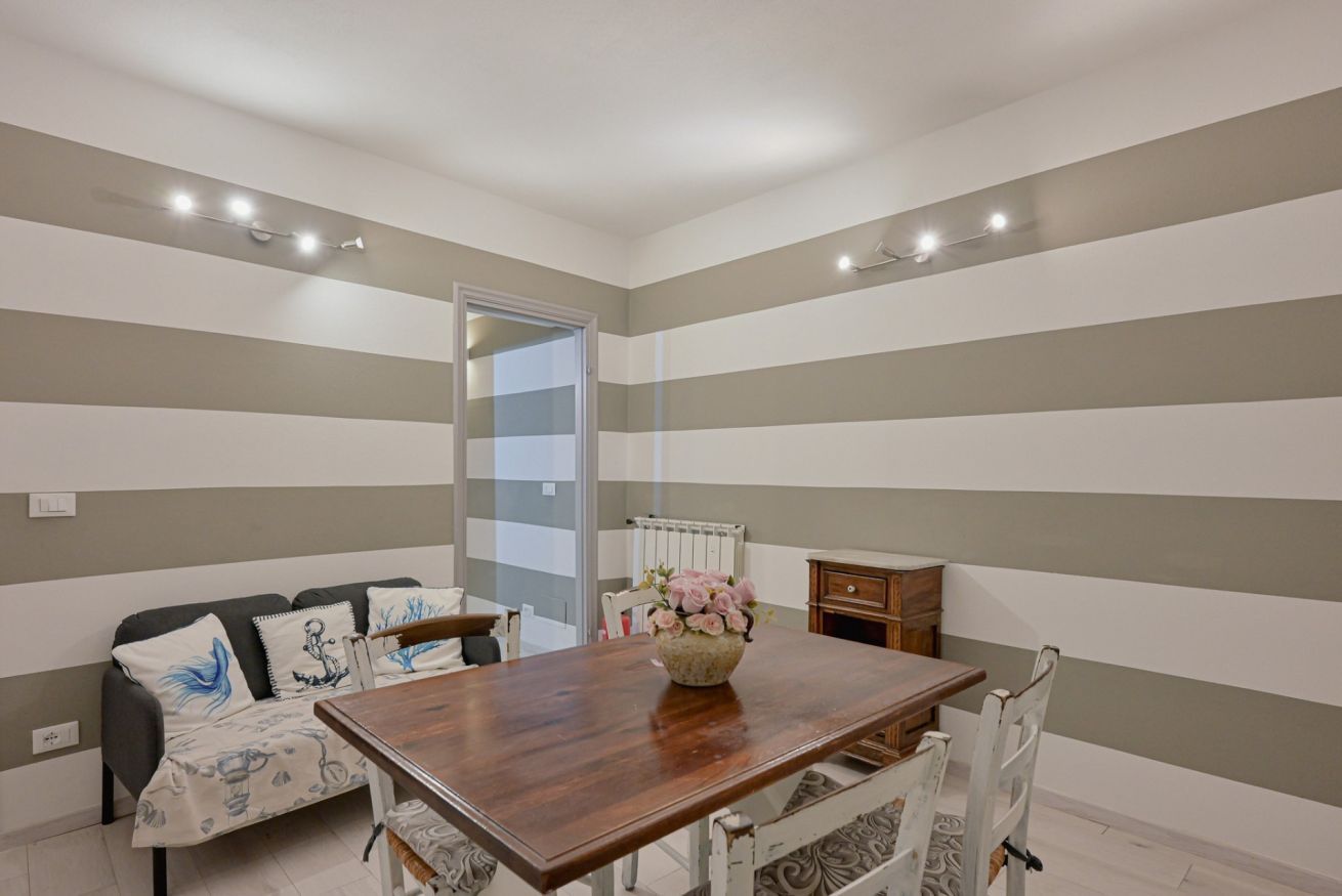 A room with a striped wall, a wooden dining table, a sofa, and a radiator.
