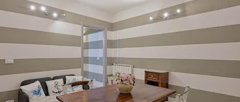 A room with a striped wall, a wooden dining table, a sofa, and a radiator.