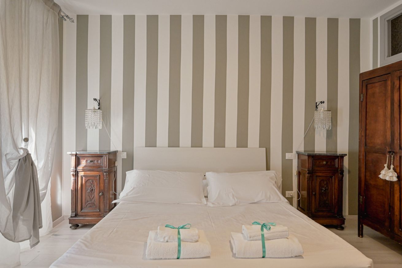 A hotel room with a bed, two nightstands, a wooden wardrobe, and striped wallpaper.