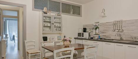 Een moderne keuken met witte kasten, een eettafel met stoelen, een magnetron en een spoelbak.