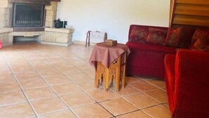 A cozy living room with a fireplace, wooden ceiling beams, a red sofa, and a tiled floor. - Vacation home for 6 in a quiet location (Saint-Cybranet)