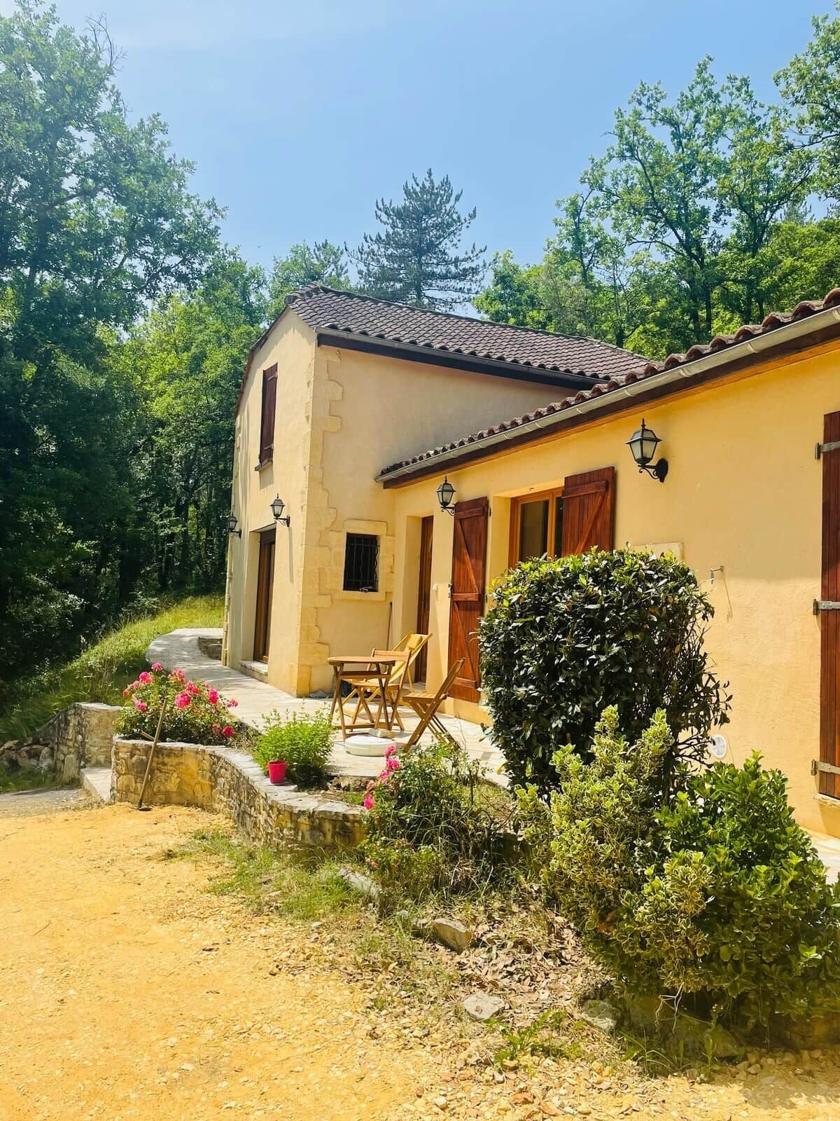 Ein zweistöckiges Gebäude mit einem Ziegeldach, einer kleinen Veranda mit Tisch und Stühlen und einem Garten mit Teich und Pflanzen.