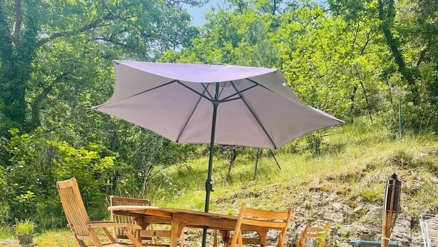 An outdoor patio with a wooden table and chairs, a large umbrella, and a stone wall. - Vacation home for 6 in a quiet location (Saint-Cybranet)