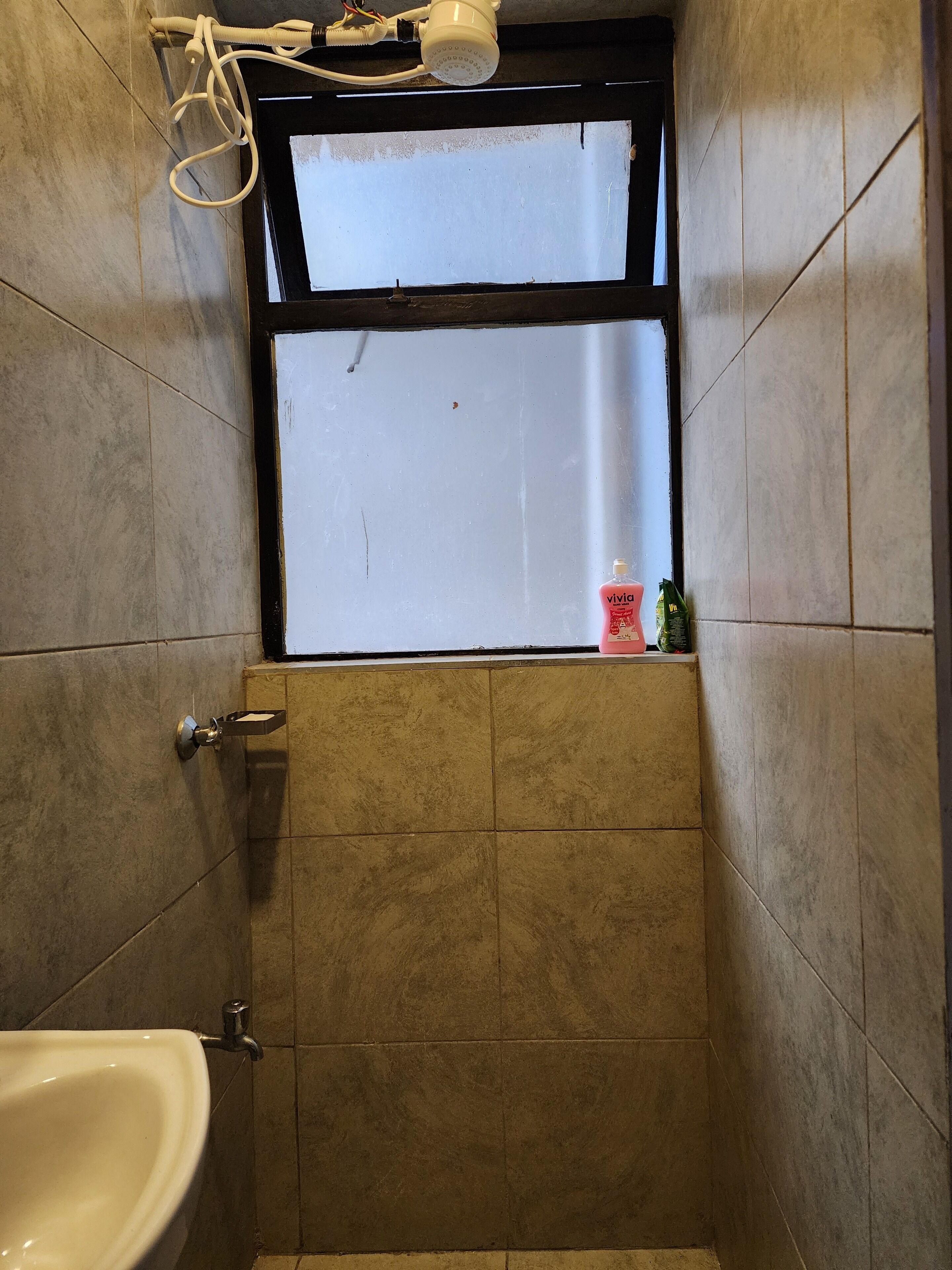 A bathroom with a window, a showerhead, a sink, and toiletries.