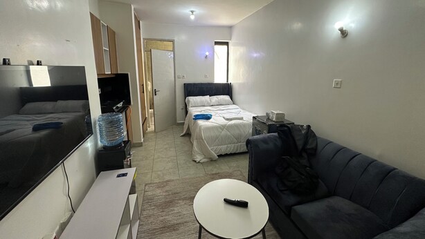 A hotel room with a bed, a sofa, a small table, a TV, and a water dispenser.