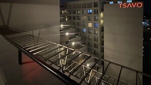 A modern building with a prominent 'TSAVO' sign in red letters, a glass railing, and a view of a multi-story structure with illuminated windows.