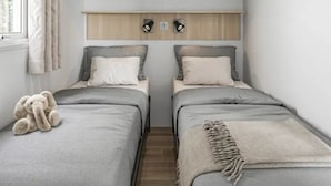 Quarto com duas camas, uma janela com cortinas, um armário sobre as camas e um urso de pelúcia em uma das camas.
