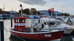 Ein Yachthafen mit verschiedenen anlegenden Booten, darunter ein rotes Boot mit der Aufschrift 'NIE 4' und ein weißes Boot mit der Aufschrift 'ANDI III'.