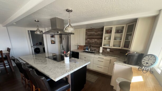 A modern kitchen with a central island, stainless steel appliances, and a clock on the wall. - Private 3-bedroom Guesthouse with beautiful views of Kachemak Bay. (Homer)