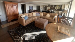 A living room with a sectional sofa, a wooden cabinet, a dining table with chairs, and a kitchen in the background. - Private 3-bedroom Guesthouse with beautiful views of Kachemak Bay. (Homer)