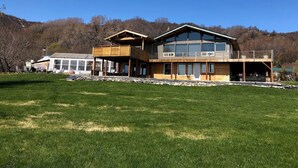 A modern two-story house with large windows, a wooden deck, and a stone foundation. - Private 3-bedroom Guesthouse with beautiful views of Kachemak Bay. (Homer)