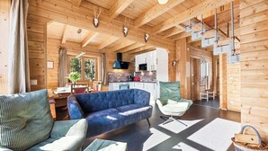 Ein Holzblockhaus-Interieur mit einer Couch, einem Sessel, einem Esstisch, einer Küchenzeile und einer Treppe.