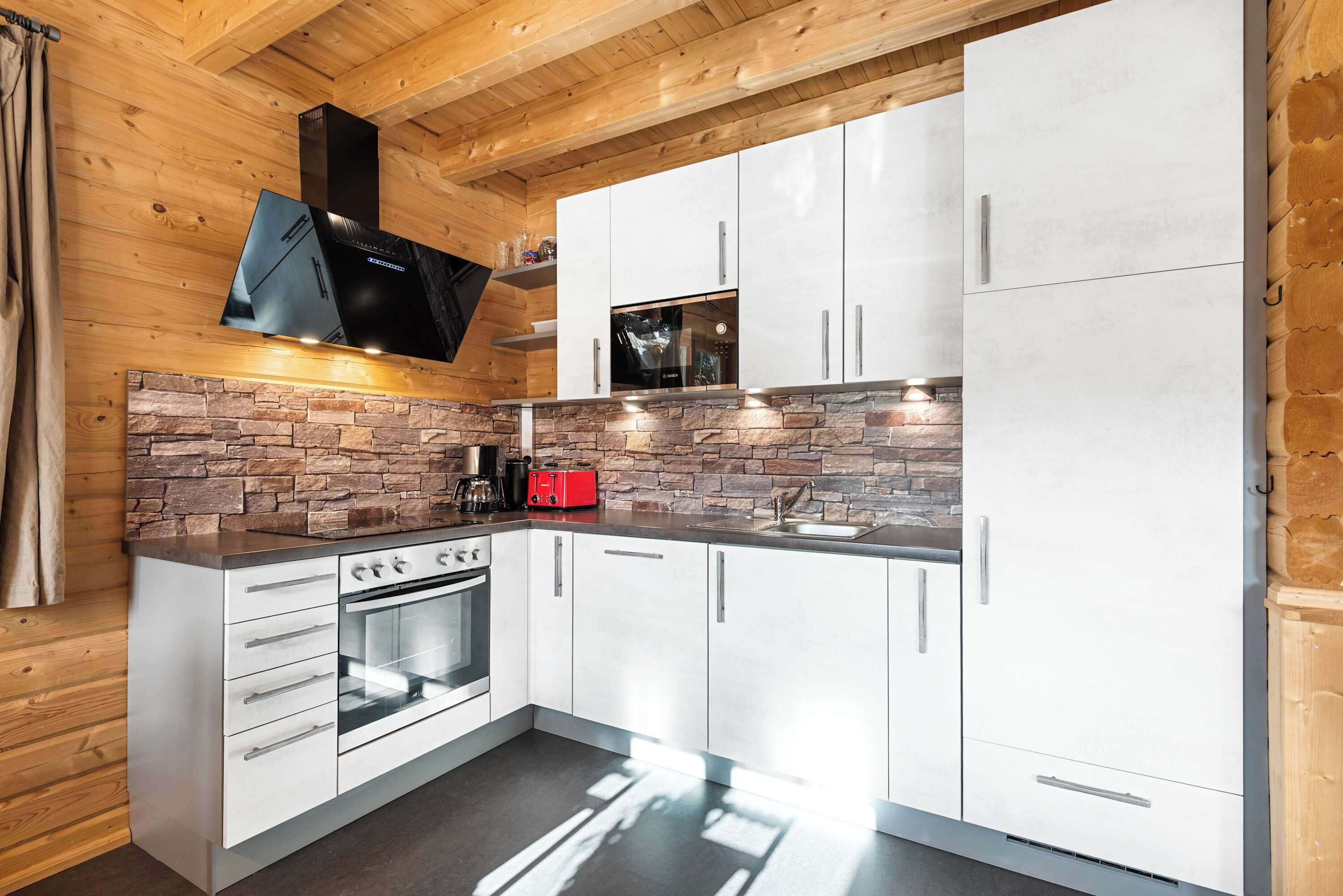Et moderne køkken med hvide skabe, en indbygget ovn og en backsplash i sten.