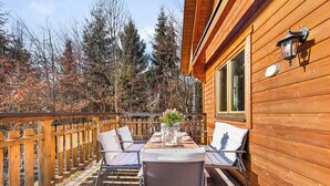 Eine Holzdielen-Terrasse mit Esstisch und Stühlen, umgeben von einer Holzhütte mit Fenster und einer Wandleuchte.