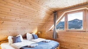 Ein Zimmer mit Holzwandverkleidung, einem Bett, einem Fenster mit Bergblick und einer geneigten Decke.