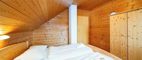 A wooden cabin room with a bed, a wardrobe, and a ceiling light.
