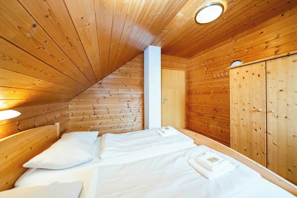 A wooden cabin room with a bed, a wardrobe, and a ceiling light.