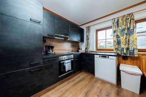 Eine kompakte Küche mit dunklen Schränken, einer Holz Arbeitsplatte, einem eingebauten Backofen, einem Geschirrspüler und einem Fenster mit gemusterten Vorhängen.