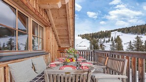 A wooden deck with a table set for dining, overlooking a snowy mountain landscape.
