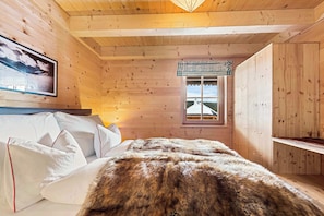 A wooden cabin room with a bed, pillows, a fur blanket, a framed picture, and a window with a view. - Chalet Lachtal | Ski-in/out | Fireplace | Balcony (Schönberg-Lachtal)