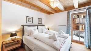 A bedroom with a wooden ceiling, a bed with white bedding, a nightstand with a lamp, and a window with curtains.
