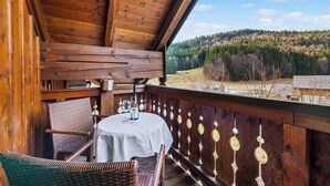 Un balcón de madera con una mesa y sillas, con vistas a un paisaje boscoso.