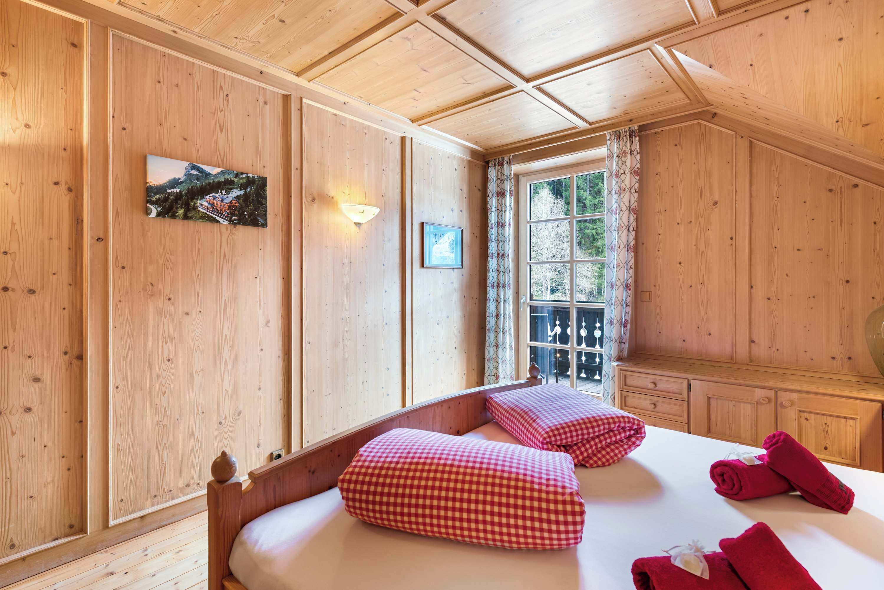 A wooden-paneled room with a bed, pillows, a window with curtains, and a wall-mounted picture.
