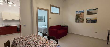 Una stanza con un letto, un divano rosso, un tavolo da pranzo, un angolo cottura e un lampadario.