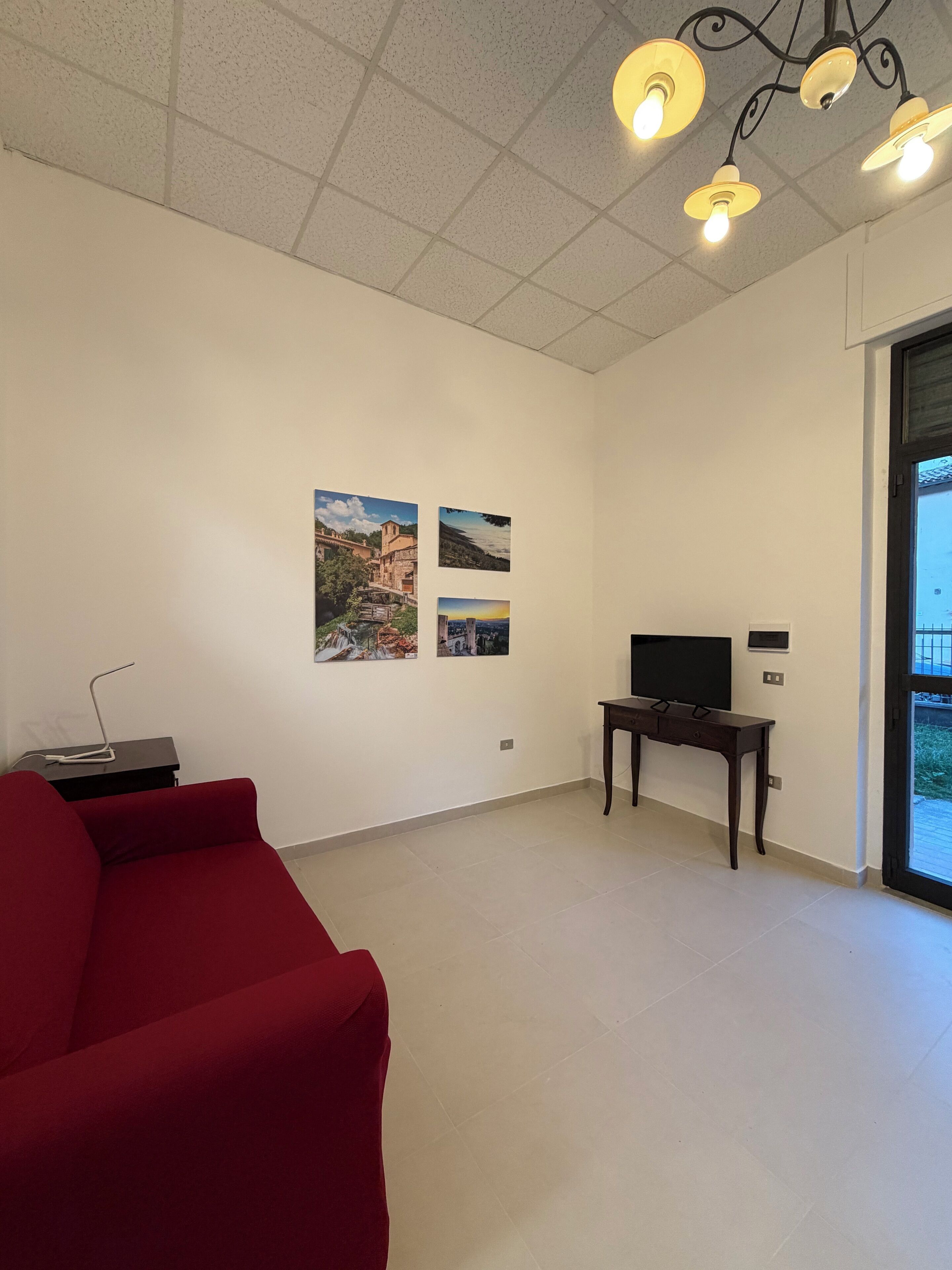 Ein geräumiges Zimmer mit einem roten Sofa, einem Flachbildfernseher auf einem Schrank und drei gerahmten Fotos an der Wand.