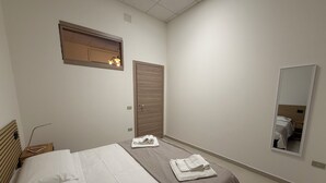A bedroom with a bed, a wooden wardrobe, a mirror, and a small window with light fixtures. - Guest House Colfiorito by Ospitaci-appartamento (Colfiorito)