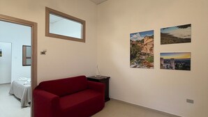 A room with a red sofa, a small table, a ceiling light fixture, and two framed pictures on the wall. - Guest House Colfiorito by Ospitaci-appartamento (Colfiorito)