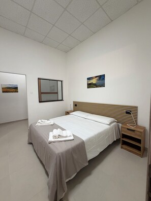 Habitación de hotel con una cama, una mesita de noche, una lámpara de pared y dos cuadros enmarcados.
