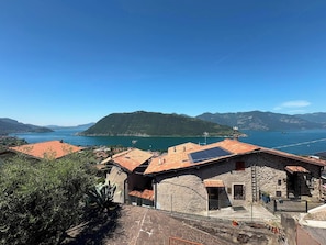 Un village côtier aux bâtiments en pierre, sous un ciel bleu azur, offrant une vue sur la mer et les montagnes.