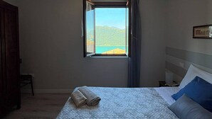 A bedroom with a bed, a window with a view, a wooden wardrobe, and a chair. - La Casa della Nonna - Two Bedroom House, Sleeps 6 (Sale Marasino)