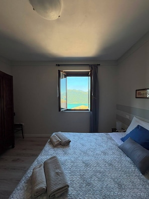 Une chambre à coucher avec un lit, une fenêtre donnant sur un beau paysage, une armoire en bois et une chaise.