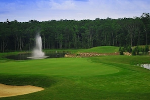 A golf course with a water hazard, sand bunkers, and a forested backdrop.
