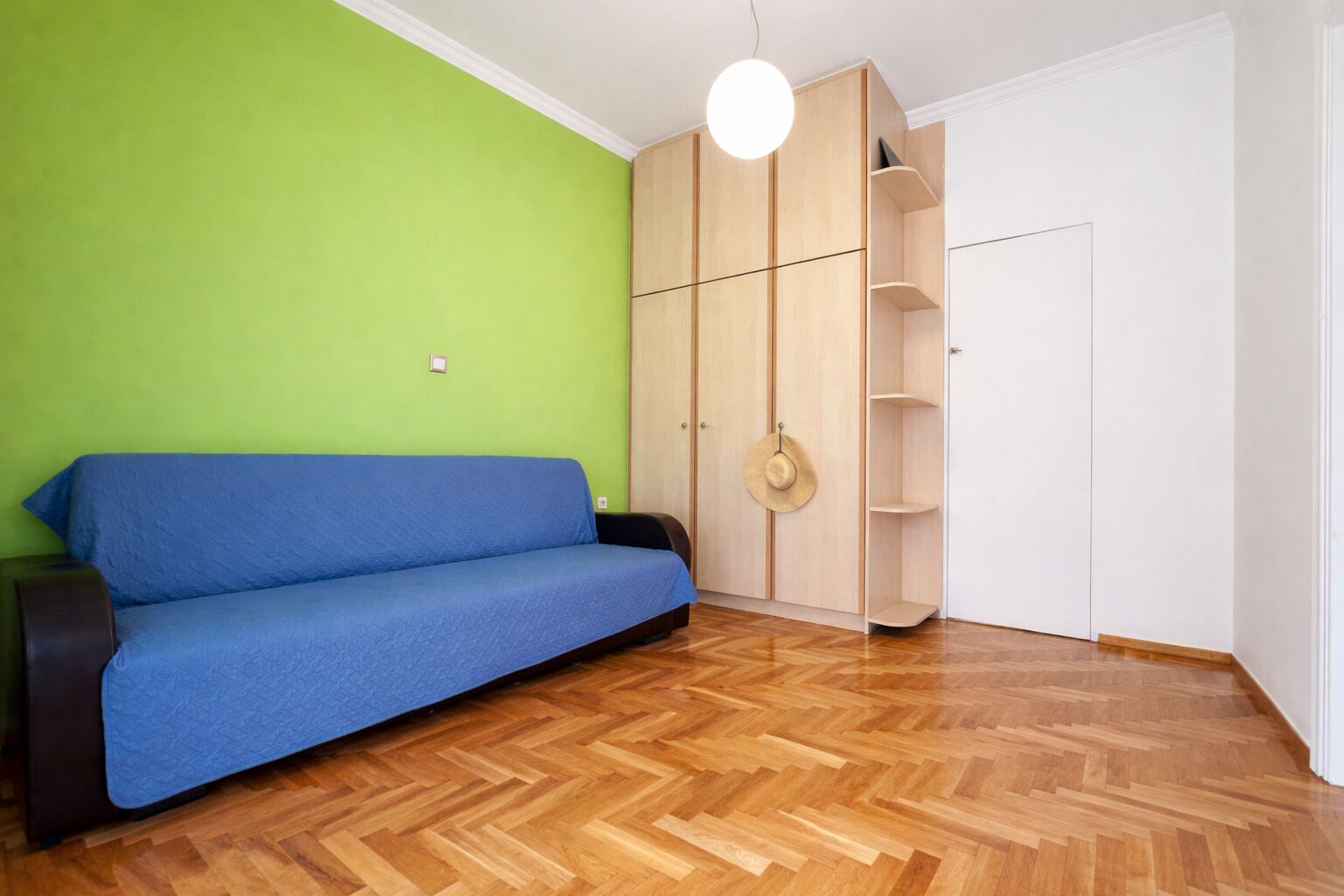 A room with a blue sofa, wooden wardrobe, and a green wall.