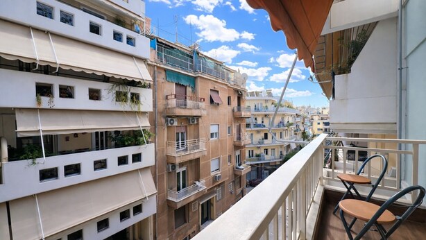 Un balcó amb vistes a edificis d'altes plantes, una barana i un parell de cadires.