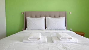 Un llit amb dues almoines i dues tovalloles doblegades, una tauleta de nit de fusta i una paret verda.