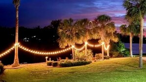 A nighttime outdoor area with palm trees, a grassy lawn, and string lights. - Resort style 5-bedroom lake house with white sand beach, pool, and pool house. (Douglas)