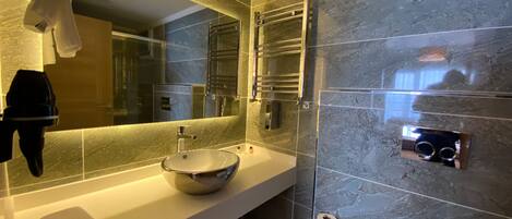 A modern bathroom with a large mirror, a vessel sink, a towel rack, and a towel dispenser.
